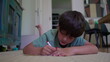 © Marco - Boy lies on floor concentrating while drawing with red marker, indoor environment with furniture and patterned artwork in background