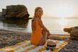 © mary_markevich - beautiiful smiling happy young woman sitting on beach by sea tanning dressed in orange swimsuit, summer fashion vacation accessories trend