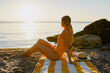 © mary_markevich - beautiiful smiling happy young woman sitting on beach by sea tanning dressed in orange swimsuit