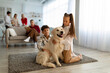 © Prostock-studio - Cute children with golden retriever dog sitting on floor at home, their parents and grandparents on background. Big extended family spending time together in living room