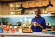 © DC Studio - Portrait of smiling black woman serving fresh coffee in a mug before preparing toast and pastry for breakfast. Enjoying calm morning at home, surrounded by kitchenware and healthy food.