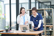 © Thitisak - Two female healthcare workers, one in blue scrubs and another in a white lab coat, are collaborating and reviewing patient charts on a clipboard and tablet. They are engaged in a professional discussi