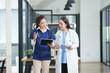 © Thitisak - Two female healthcare workers, one in blue scrubs and another in a white lab coat, are collaborating and reviewing patient charts on a clipboard and tablet. They are engaged in a professional discussi