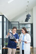 © Thitisak - female doctor in a white lab coat and a medical assistant in blue scrubs are sitting at a wooden desk, collaborating and reviewing medical documents or X-rays. Both are wearing stethoscopes, reflectin