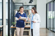 © Thitisak - Two female healthcare workers, one in blue scrubs and another in a white lab coat, are collaborating and reviewing patient charts on a clipboard and tablet. They are engaged in a professional discussi