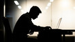 © Bakti - Silhouette of a man working on a laptop computer at night.