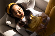 © Wavebreak Media - Asian woman reclining on sofa at home wearing mustard overalls holding dusty pink headphones