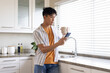 © Wavebreak Media - Adult Asian man leaning at kitchen counter, holding ceramic mug and checking phone in striped shirt