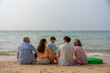 © Thitiporn - Happy multi-generational Asian family sitting on the beach with their backs to the camera, raising hands and enjoying fun vacation moment together by the sea. family, beach, vacation, summer. elderly