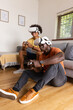 © wavebreak3 - Diverse male friends playing virtual reality game next to sofa at home with wireless controllers