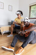 © wavebreak3 - Two friends playing vr games in living room on sofa wearing headsets with controllers
