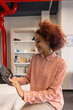© wavebreak3 - Female office worker in pink blouse tapping tablet at desk near bookshelf, red pipe overhead
