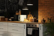 © Pixel-Shot - Interior of stylish kitchen with stove, utensils and glowing lamps at night