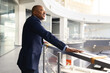 © Anastasiya - Black mature businessman leaning on office balcony railing, looking ahead with confidence and vision, executive lifestyle in modern corporate architecture