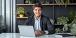 © Ilja - Confident Young Hispanic Entrepreneur Smiling at Office Desk in Energetic Work Ambiance
