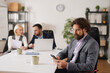 © Stockphotodirectors - A business team works in a meeting room discussing ideas and plans for success. One member checks their phone while others collaborate at the table.