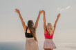 © svetograph - Two women are standing on a beach, one wearing a pink top and the other wearing a black top. They are both holding their hands up in the air, as if they are celebrating something. The sky is clear.