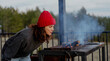 © olezzo - Young woman in red hat blowing fire in barbecue grill on countryside house terrace