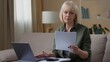 © Yuliia - Serious Caucasian old woman with papers documents looking laptop confused senior female retired lady checking data letters income budget expenses with computer at home homeowner paperwork indoors