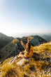 © maxbelchenko - A young woman with hiking backpack stands on mountain trail on sunny day. Female hiker with a yellow backpack enjoys mountain scenery at sunset. Concepts of adventure, freedom. Active lifestyle.