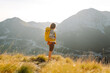 © maxbelchenko - A young woman with hiking backpack stands on mountain trail on sunny day. Female hiker with a yellow backpack enjoys mountain scenery at sunset. Concepts of adventure, freedom. Active lifestyle.