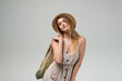 © Volodymyr_sh - Stylish young woman posing with reusable grocery bag and straw hat, eco friendly summer lifestyle portrait on gray background