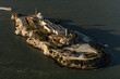 © AmazingAerialAgency - Aerial view of Alcatraz Island, a somber fortress rising from the shimmering bay waters, its weathered walls echoing tales of isolation and resilience, San Francisco, California, United States.