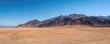 © TommyNa - Wide empty desert plain with distant rugged mountain range and clear blue sky creating vast open space and minimal natural scenery for climate environment and background concepts