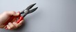© pvl0707 - Close-up view of a hand holding red pliers while trying to open a black battery box on a gray background during a task in a workspace