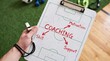 © The Stock Hub - A coach's hand holding a clipboard with a soccer field diagram and coaching strategy written in red marker.
