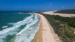 © AmazingAerialAgency - Aerial view of waves crashing onto the sandy shore next to the lush green vegetation with Tukkee Sandblow and Indian Head in the background, K'Gari Fraser Island, Queensland, Australia.