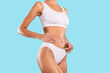 © Prostock-studio - Close up shot of unrecognizable fit woman wearing lingerie posing isolated on blue studio background, touching body. Torso of slim female with flat belly in white underwear top bra and panties, banner