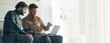 © Prostock-studio - Two men sit together in a modern office space focused on a laptop. They engage in conversation, sharing ideas while collaborating on a project. Sunlight fills the room.