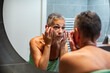 © Marko Geber - Mature woman examining face in home bathroom mirror