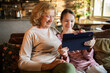 © Geber86 - Senior woman and teen girl using tablet on sofa at home