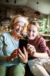 © Geber86 - Grandmother and granddaughter with face masks taking selfie at home