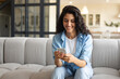 © Prostock-studio - Young brunette woman using cellphone on sofa, checking email, having online video chat at home, copy space. Millennial Caucasian female posting in social media, messaging to friend indoors