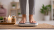 © Yurij - Person standing barefoot on a digital scale in a cozy home setting with lit candles and plants for a healthy lifestyle and self-care routine concept