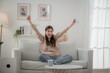 © surachetkhamsuk - Happy young woman watching TV and cheering on sofa at home.