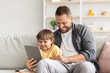 © Prostock-studio - Distant communication. Young father and his cute little son video chatting with relatives via digital tablet, sitting together on sofa and smiling to gadget, empty space