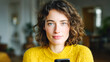 © Yurij - Woman with curly hair and green eyes wearing a cozy yellow sweater looking confidently at the camera with a blurred living room background behind her