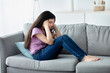 © Prostock-studio - Unhappy teen girl holding her head in despair, feeling depressed, sitting on sofa at home, copy space. Indian asdolescent going through difficult times, having mental problems or mood disorder