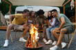 © Prostock-studio - Group of cheerful diverse friends spending time near bonfire, having camping vacation with RV, watching video on smartphone, chatting and having fun outdoors in summer