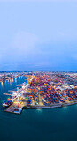 a busy deep-water cargo container port terminal during the twilight blue hour. Logistics center illuminated by industrial lights with gantry cranes and shipping vessels. Global trade infrastructure.