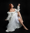 © faestock - Full length portrait beautiful female model with red hair wearing a antique white historical ghost bride wedding dress gown. classical elegant sitting pose, Isolated figure on dark studio background