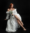 © faestock - Full length portrait beautiful female model with red hair wearing a antique white historical ghost bride wedding dress gown. classical elegant sitting pose, Isolated figure on dark studio background