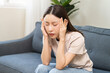 © KMPZZZ - Depressed anxiety asian young woman frustrated hand on head, touching her temples, suffering stressed, sick, tired, crisis on sofa from headache, migraine pain tension problem health care concept.