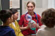 © pressmaster - Caucasian young adult woman demonstrating medical resuscitator mask to group of attentive children in classroom setting, children watching closely as instructor explains equipment