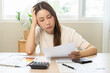 © KMPZZZ - Debt and financial concept, stressed asian young woman have a headache while female calculate expenses, income and expenses, looking bills of credit card for payment or payday on table at home office.