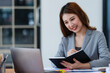 © Songsak C - Portrait of smiling Asian businesswoman working on laptop at workplace in modern office.